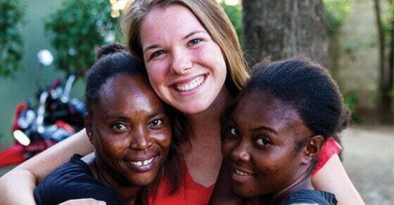 A volunteer smiles with two Haitian women