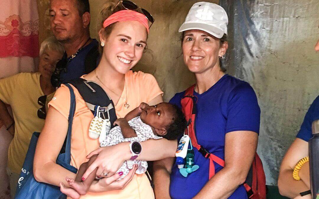 Volunteers walk around a market and smile with a baby.
